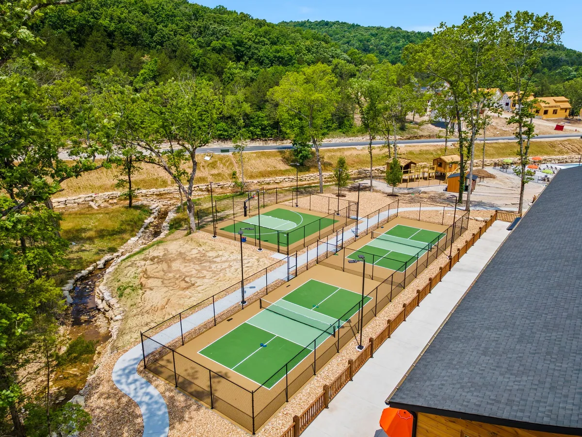 Well-maintained tennis courts surrounded by lush greenery, with a play area visible in the background. The space is inviting for both friendly matches and energetic family recreation, emphasizing the active, group-friendly amenities on offer.