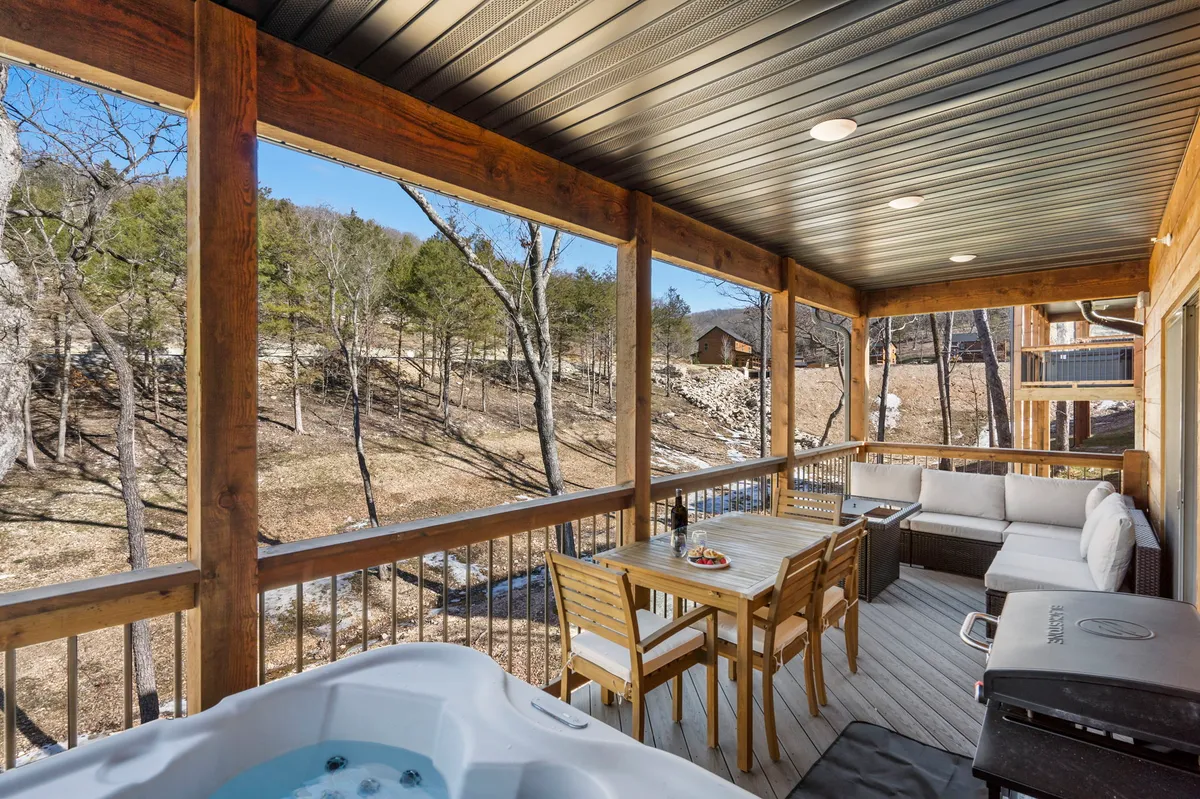 An exterior deck area with a hot tub, dining table, and comfortable seating. The space is designed for outdoor dining, relaxation, and socializing while enjoying the views and atmosphere of the deck.
