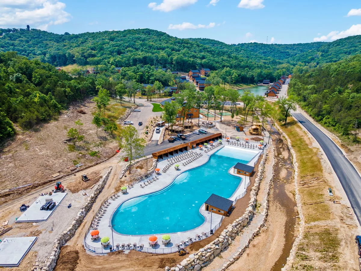 A spacious outdoor swimming pool set against rolling green hills, with modern cabanas and lounge chairs lining the deck. The scene conveys a relaxed, recreational atmosphere ideal for seasonal enjoyment and community gatherings.