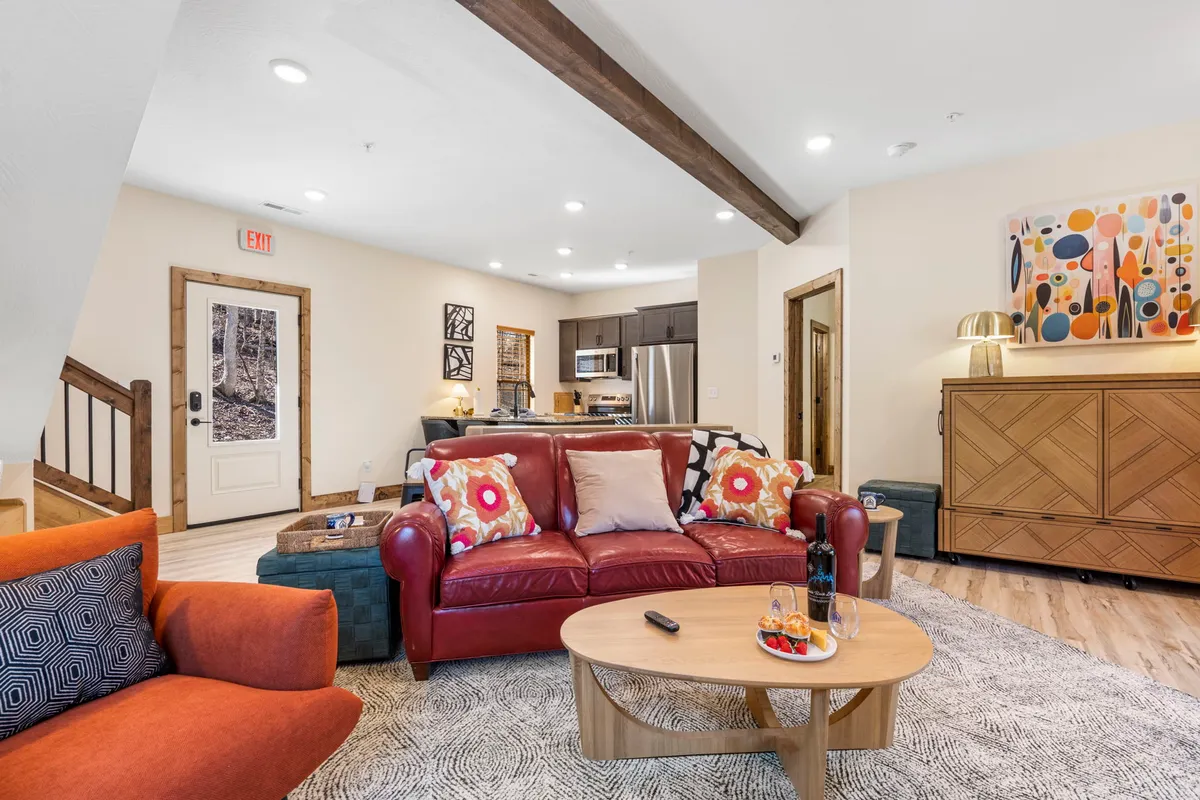 The image showcases the inviting interior of The Mod Lodge cabin, with a plush red leather sofa as the focal point. Vibrant artwork adorns the wall, and a sturdy wooden coffee table sits atop a textured rug. The space feels cozy and welcoming, perfect for relaxing, playing games, or enjoying a glass of wine with loved ones.