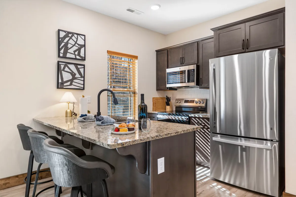 A modern kitchen featuring a granite countertop, stainless steel appliances, and bar stools, with inviting artwork on the wall. The area exudes a welcoming vibe for both casual dining and entertaining family or friends.