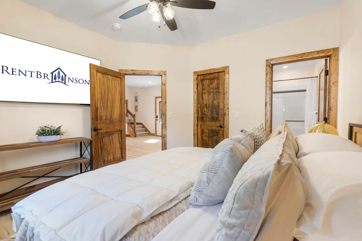 A king bedroom featuring a comfortable bed adorned with decorative pillows, a wall-mounted TV for entertainment, and rustic wooden doors. The space looks serene and offers modern amenities for unwinding in privacy.