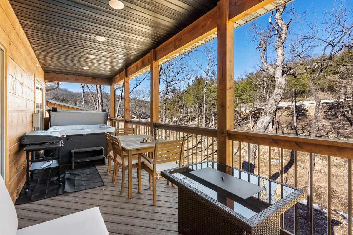 This image shows an inviting outdoor deck area featuring a hot tub, comfortable seating, a wooden railing, and sweeping views of the natural landscape. The scene is set up for relaxation or socializing, with the hot tub as a central feature and plenty of space for guests to lounge or dine outdoors.