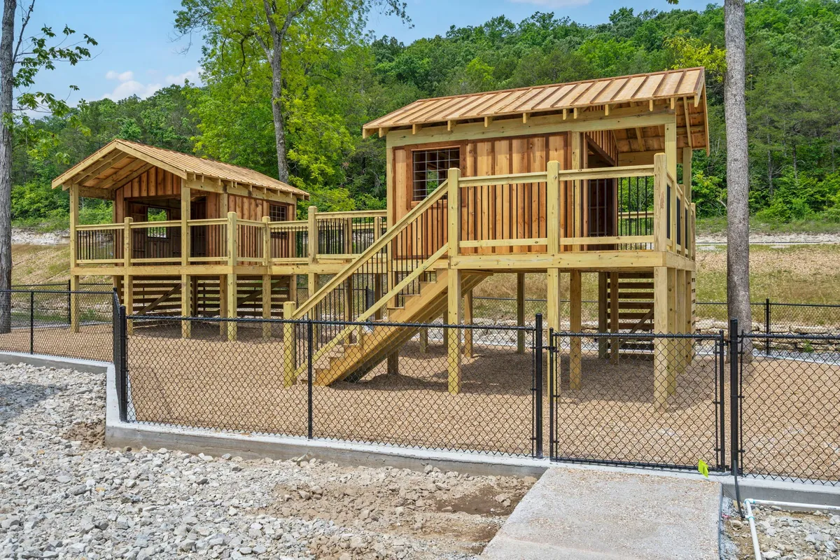 The photo showcases two wooden, treehouse-like structures on stilts surrounded by greenery and a fenced play area, with children engaged in imaginative play and exploration. The mood is joyful and adventurous, embodying active family fun outdoors.