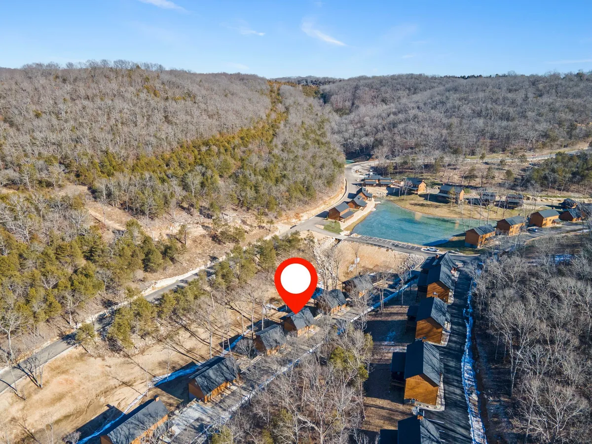 A cluster of wooden cabins sits in a serene landscape of rolling hills, open green spaces, and a reflective water body. The setting is perfect for sunset strolls, fishing, or simply enjoying the peacefulness of nature together.