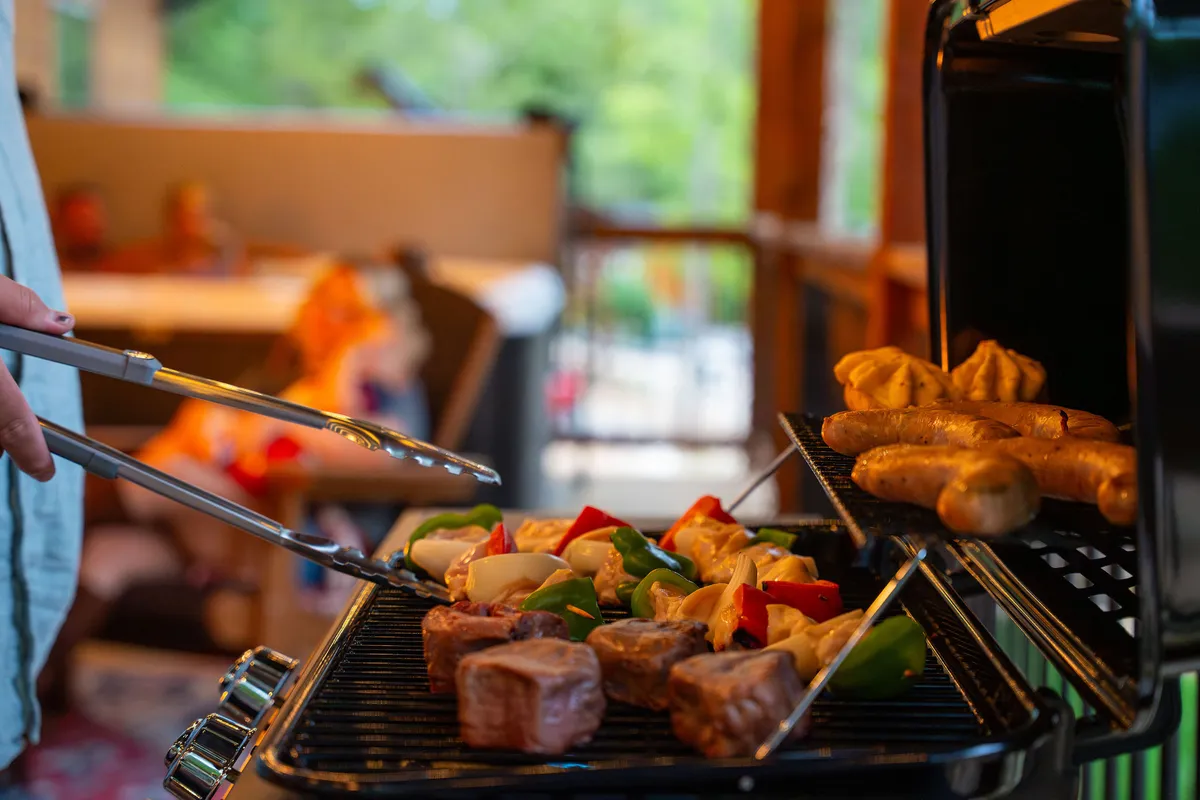 A lively scene of a person grilling food indoors, with a seating area visible in the background. The grill is the focal point, with the aroma of food and a sense of camaraderie surrounding the space—perfect for memorable meals and shared laughter.